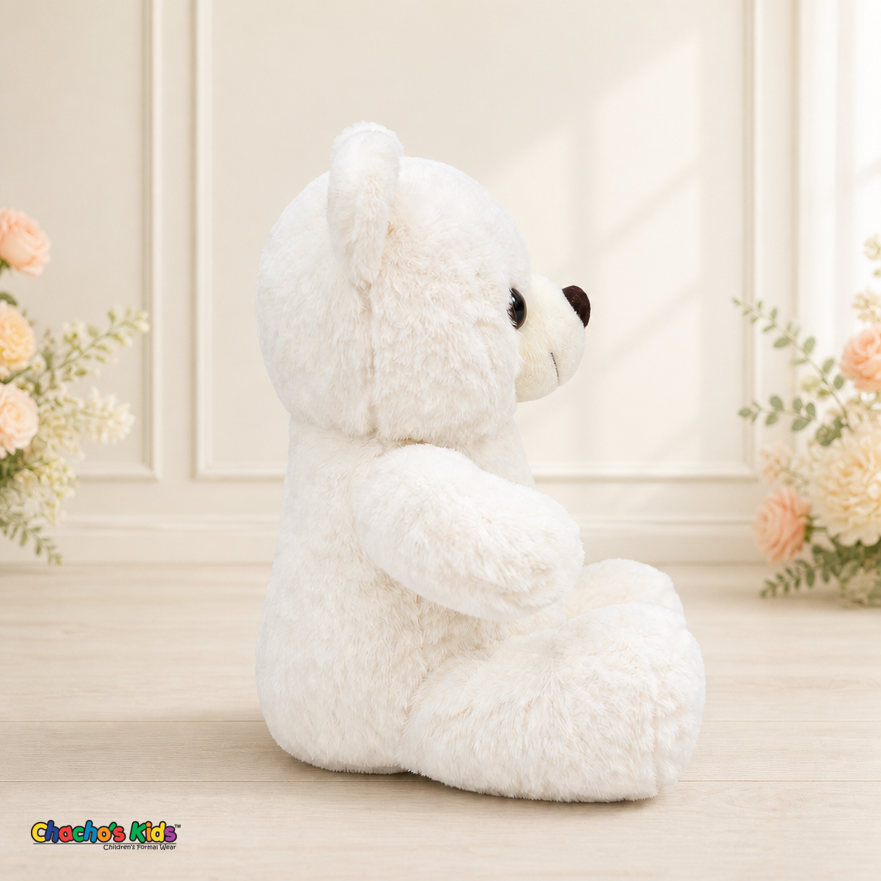 Side view of white Mini Quince teddy bear dress display in elegant cream interior with soft blush flowers