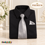 Neatly folded premium black boys dress shirt with a silver satin tie and triangular silver pocket square on an elegant ivory display.