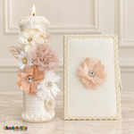 Lit ivory baptism candle with dusty-blush and peach flowers beside its coordinating floral Bible